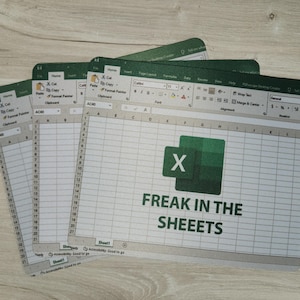 May include: A stack of green and white mouse pads featuring a mock-up of a spreadsheet program. The Excel logo is visible, along with the text "FREAK IN THE SHEEETS". The pads are arranged on a light wood-grain surface.
