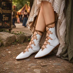 May include: A pair of white ankle boots featuring a pointed toe and a cutout design along the sides. The boots are secured with thin brown laces that crisscross up the front and wrap around the ankles, paired with a layered beige lace skirt.