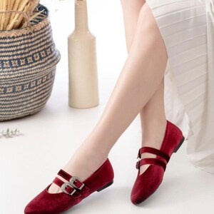 May include: A pair of burgundy velvet flats with silver buckles. The shoes have a pointed toe and a low heel.