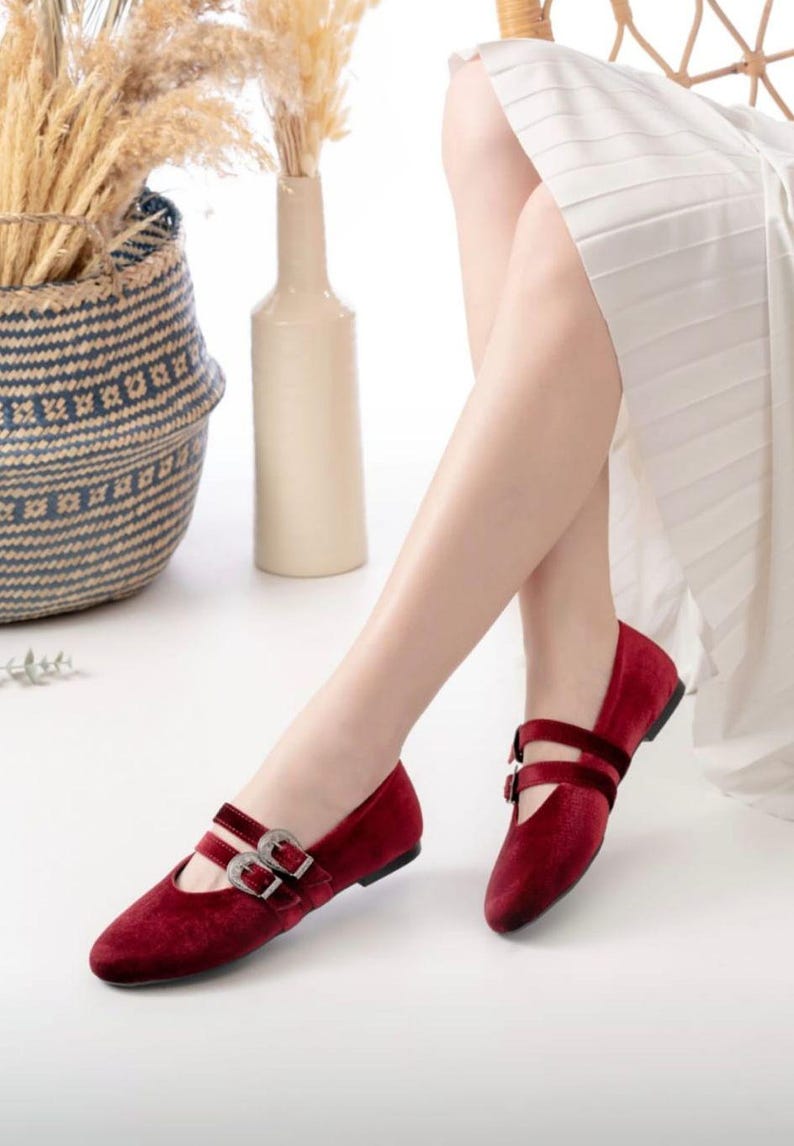 May include: A pair of burgundy velvet flats with silver buckles. The shoes have a pointed toe and a low heel.
