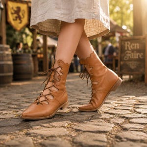 May include: A pair of tan leather lace-up boots featuring a scalloped top edge, a pointed toe, and a low stacked heel. The boots have a front lacing system with thin brown laces that extend from the toe area up to the scalloped ankle opening.
