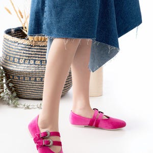 May include: A pair of pink velvet flats with silver buckles. The shoes have a pointed toe and a strap across the instep.