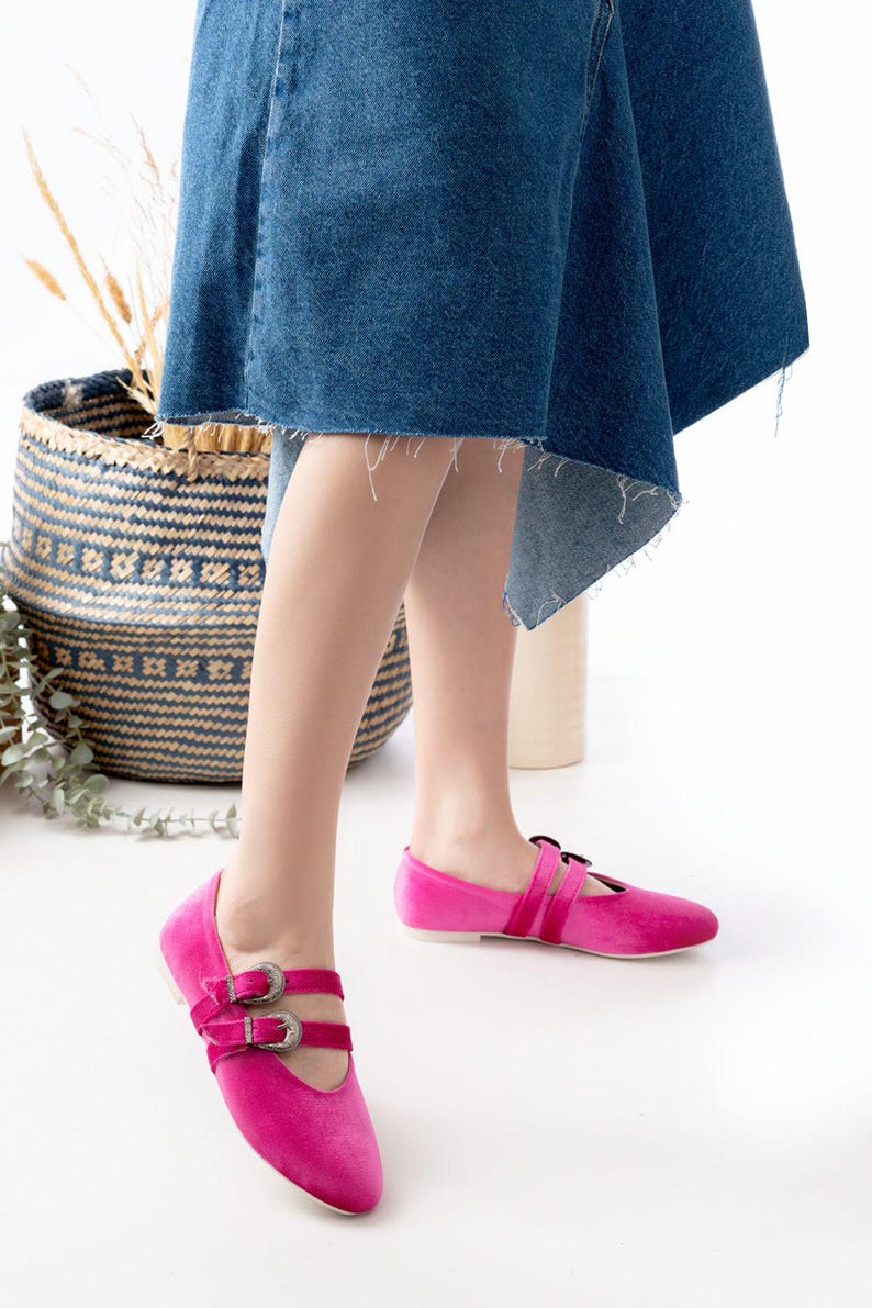 May include: A pair of pink velvet flats with silver buckles. The shoes have a pointed toe and a strap across the instep.
