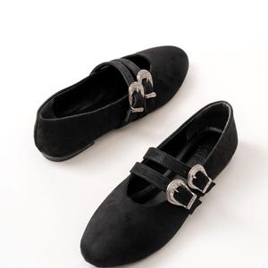 May include: A pair of black suede flats with silver buckle accents. The shoes have a pointed toe and a low heel.