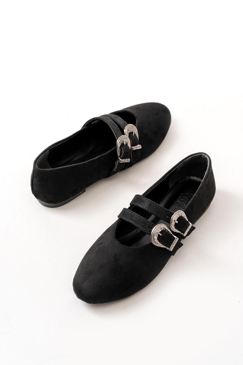 May include: A pair of black suede flats with silver buckle accents. The shoes have a pointed toe and a low heel.