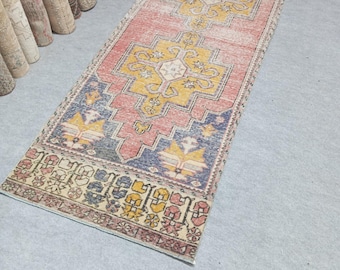 May include: A rectangular, vintage-style runner rug with a central design in yellow and white, set against a faded red background. The rug features blue and yellow geometric patterns at each end, with a decorative border.