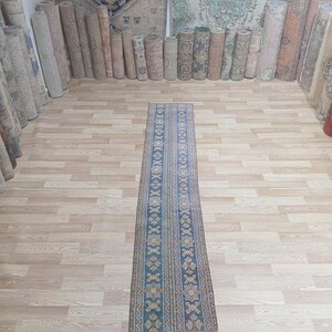 May include: A long, narrow runner rug with a blue background and intricate geometric patterns in shades of blue, orange, and yellow. The rug has a fringe on both ends.