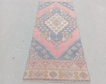 May include: A rectangular, vintage-style rug with a central pink diamond pattern, framed by navy blue and beige geometric designs. The rug has a distressed look, suggesting it is handmade or antique.