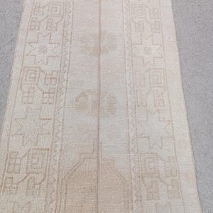 Può includere: Un tappeto runner beige e marrone chiaro con un motivo geometrico. Il tappeto presenta un campo centrale e bordi dettagliati. Il tappeto è realizzato in un materiale tessuto e ha un aspetto vintage o antico.