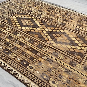 Può includere: Un tappeto a motivi marroni e beige con intricati disegni geometrici. Il tappeto ha un aspetto e una sensazione tradizionali, tessuto a mano.