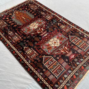 May include: A rectangular, hand-knotted rug with a dark background and intricate geometric patterns. The rug features a central design with floral and vase motifs in shades of red, blue, and cream, surrounded by a detailed border. The rug's dimensions are not visible.