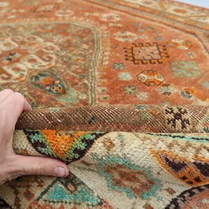 May include: A vintage rug with a colorful geometric pattern in shades of orange, brown, white, and turquoise. The rug is folded in half, revealing the back side.