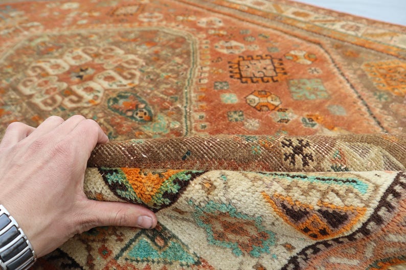 May include: A vintage rug with a colorful geometric pattern in shades of orange, brown, white, and turquoise. The rug is folded in half, revealing the back side.