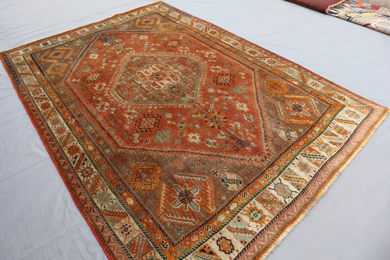 May include: A vintage rug with a red, orange, and brown color scheme. The rug has a central medallion with intricate floral and geometric patterns. The border is a cream color with a repeating pattern of stylized leaves and flowers.