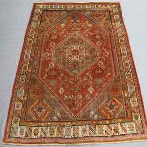 May include: A vintage rug with a red, orange, and brown color scheme. The rug has a central diamond-shaped design with intricate floral patterns and a border with geometric motifs.