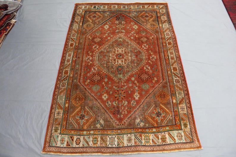May include: A vintage rug with a red, orange, and brown color scheme. The rug has a central diamond-shaped design with intricate floral patterns and a border with geometric motifs.