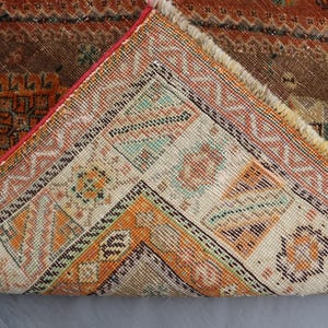 May include: Close-up of the back side of a vintage rug with a geometric pattern in shades of brown, orange, and white.