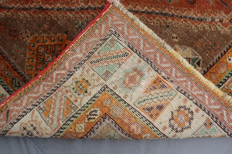 May include: Close-up of the back side of a vintage rug with a geometric pattern in shades of brown, orange, and white.