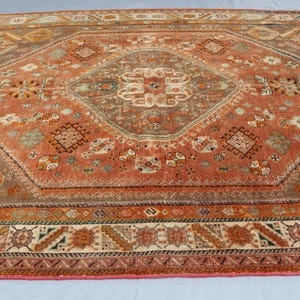 May include: A vintage rug with a geometric pattern in shades of red, brown, and cream. The rug has a central diamond shape with intricate details and a border with a repeating design.