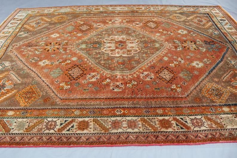 May include: A vintage rug with a geometric pattern in shades of red, brown, and cream. The rug has a central diamond shape with intricate details and a border with a repeating design.