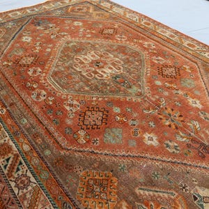 May include: A vintage rug with a geometric pattern in shades of red, orange, brown, and white. The rug has a central diamond shape with intricate details and a border with repeating motifs.