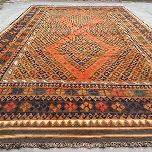 Può includere: Un tappeto persiano tradizionale con un motivo geometrico in tonalità di marrone, arancio, blu e verde. Il tappeto ha un bordo con frange ed è tessuto con dettagli intricati.