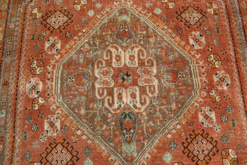May include: A vintage rug with a geometric pattern in shades of red, brown, and beige. The rug has a central medallion with a floral design and a border with repeating motifs.