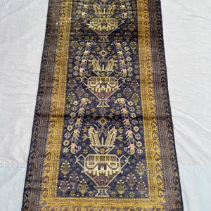 Könnte beinhalten: Ein rechteckiger, dunkelblauer Teppich mit einem komplizierten, symmetrischen Muster. Der Teppich hat ein zentrales Design mit sich wiederholenden Motiven in Gold, Braun und Rosa. Der Rand ist ein dunklerer Blauton mit einem Gold- und Braunmuster.