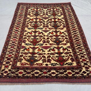 May include: A traditional Persian rug with a cream background and intricate floral patterns in shades of red, burgundy, and black. The rug has a border with a repeating floral design.