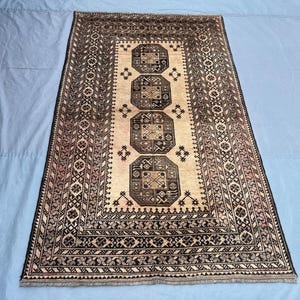 May include: Rectangular beige rug with a central pattern of three dark brown octagons. The rug has a detailed border with geometric designs in black and brown, creating a traditional aesthetic.