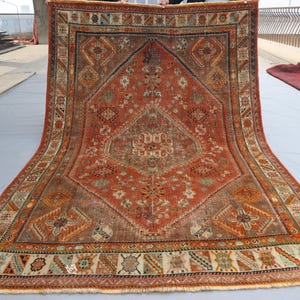 May include: A vintage Persian rug with a red, orange, and blue geometric pattern. The rug has a fringe border and is in good condition.