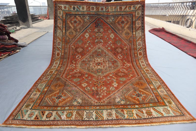 May include: A vintage Persian rug with a red, orange, and blue geometric pattern. The rug has a fringe border and is in good condition.