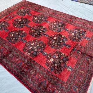 May include: A rectangular red rug with a repeating floral pattern in the center. The rug has a dark border with a geometric design. The floral pattern is in shades of brown, blue, and cream.