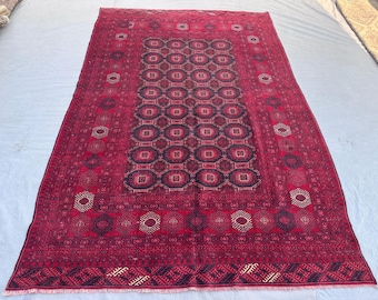 May include: A rectangular, hand-woven rug with a deep red background and intricate geometric patterns in black and beige. The central design features a series of connected octagons, framed by borders with repeating motifs. The rug's dimensions are not visible.