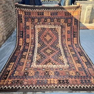 Può includere: Un tappeto tradizionale tessuto a mano con intricati motivi geometrici in tonalità di marrone, rosso, blu e bianco. Il tappeto ha un bordo con frange ed è fatto di lana.
