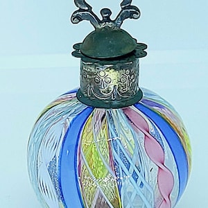 May include: A round glass bottle with a silver and bronze stopper. The bottle is decorated with colorful stripes and swirls of glass.