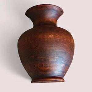 May include: A handcrafted, wooden vase with a dark brown finish. The vase has a rounded body, a flared neck, and a sturdy base. The wood grain is visible, adding to its natural aesthetic. This decorative vase is suitable for displaying flowers or as a standalone art piece.