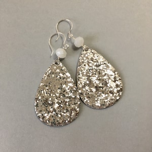 May include: Silver glitter teardrop earrings with white bead accents and silver hooks. These dangle earrings are a glamorous accessory, perfect for adding sparkle to any outfit. The earrings are lightweight and eye-catching.