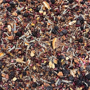 May include: Close-up of a mix of dried tea leaves and ingredients. The blend includes dark purple berries, orange citrus slices, and green stems. The tea has a variety of textures and colors, creating a visually appealing mix.