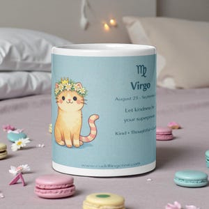 May include: A white ceramic mug with a light blue background featuring a cartoon cat wearing a flower crown. The mug has the text "Virgo" and "Let kindness be your superpower". The website www.cuddlingcrew.com is also visible.