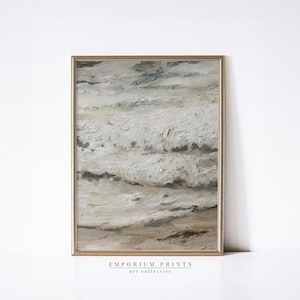 May include: A framed abstract painting with a neutral color palette. The artwork features textured brushstrokes in shades of white, beige, and gray, creating a sense of movement. The frame is a light gold color. The text "EMPORIUM PRINTS art collective" is at the bottom.