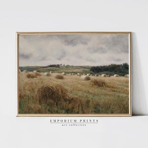 May include: A framed print depicting a rural landscape with hay bales in a field under a cloudy sky. The artwork uses a muted colour palette of beige, brown, and grey, with the text "EMPORIUM PRINTS art collective" at the bottom.