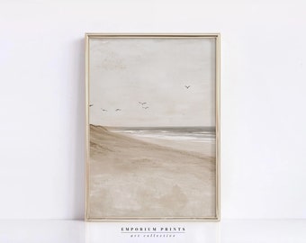 May include: A framed print depicting a minimalist beach scene with a sandy shore, a calm ocean, and a few birds flying in the sky. The print features a muted colour palette of beige, brown, and grey.