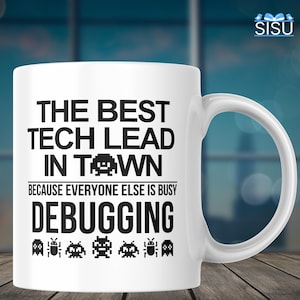 May include: White ceramic coffee mug with black text that reads "The Best Tech Lead In Town Because Everyone Else Is Busy Debugging". The text is surrounded by pixelated space invaders.