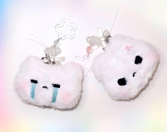 Può includere: Due ciondoli portachiavi in peluche bianco e soffice con espressioni facciali diverse. Un ciondolo ha un viso triste con disegni di lacrime blu e l'altro ha un viso scontroso con occhi neri. Entrambi i ciondoli hanno guance rosa e sono attaccati a ciondoli trasparenti a forma di stella con catene di perline.
