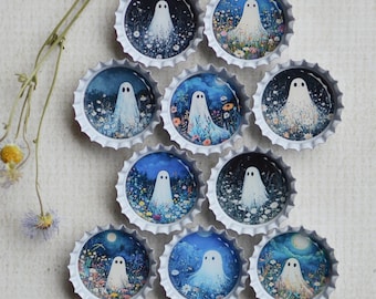 May include: A collection of bottle caps with painted ghost illustrations. Each cap features a different night scene with a white ghost figure. The caps are arranged on a white surface, with a dried flower stem nearby.