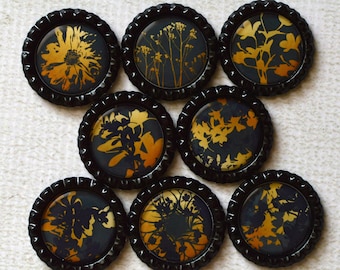 May include: Nine black bottle caps with gold floral designs. The bottle caps are arranged in a circular pattern.