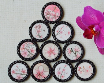 May include: A collection of ten round, black-framed floral art pieces arranged in a triangle, each featuring pink cherry blossom designs. A vibrant purple orchid flower is positioned to the right, adding a pop of color.