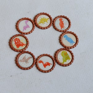 May include: Eight brown bottle caps with different dinosaur designs. Each cap features a different dinosaur in a colorful cartoon style.
