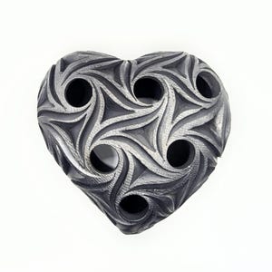 Op de afbeelding: Een hartvormige keramische plantenpot met een gedetailleerd, wervelend patroon en meerdere gaten voor drainage.